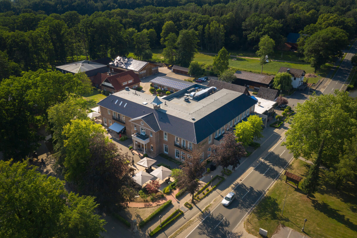 Luftaufnahme von Gut Altona: Haupthaus mit Restaurant und Terrasse, dahinter Scheune und Gästehäuser am Waldrand