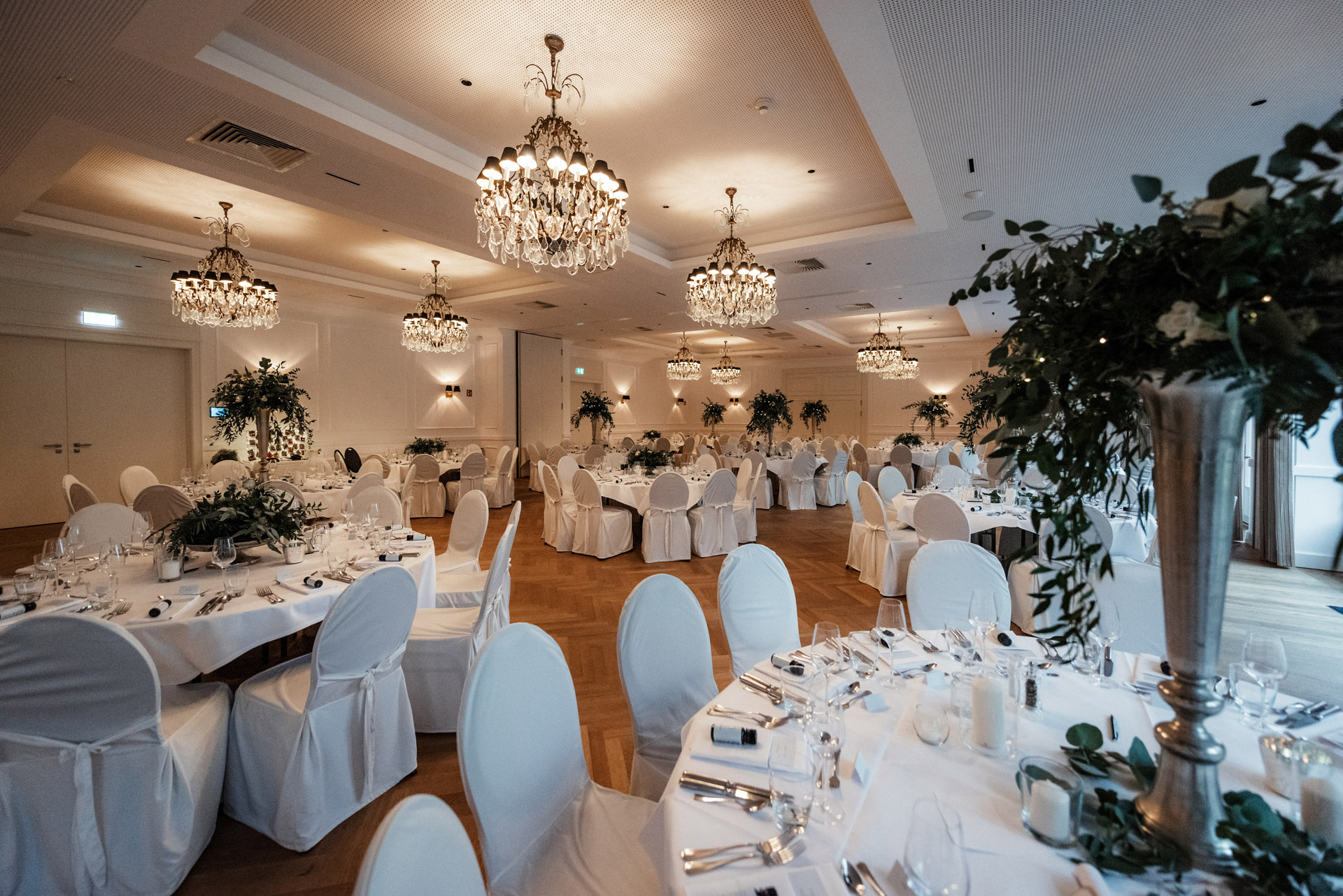 Festsaal auf Gut Altona mit hohen Blumengestecken auf den Tafeln