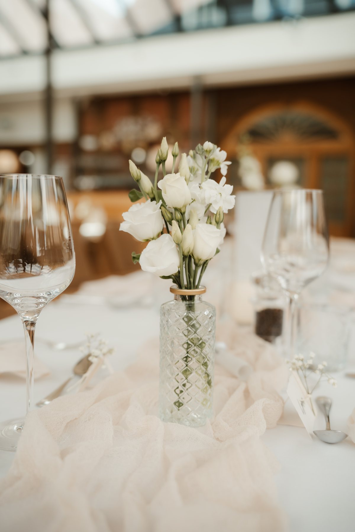 Weiße Rosen in geriffelter Glasvase auf festlich gedeckter Hochzeitstafel auf Gut Altona