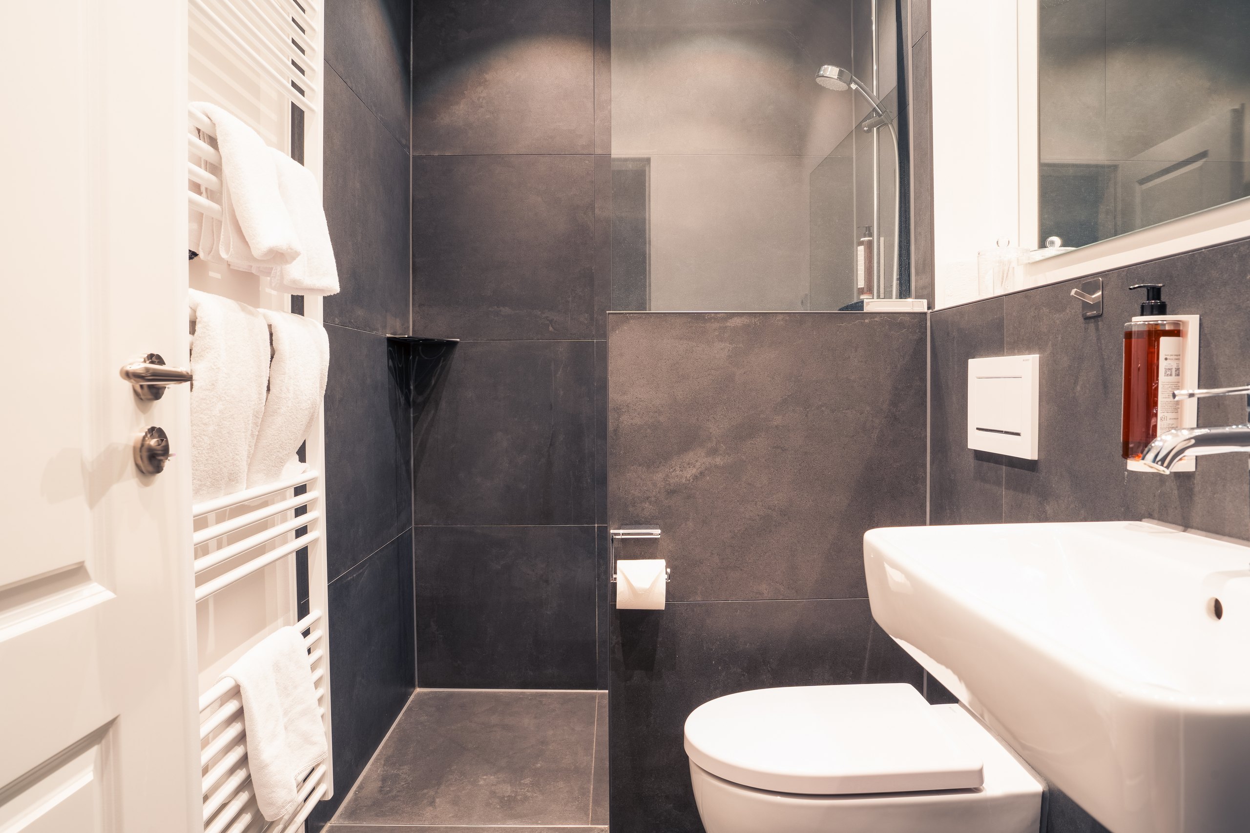 Badezimmer im Business-Doppelzimmer auf Gut Altona mit bodengleicher Dusche und dunklen Fliesen