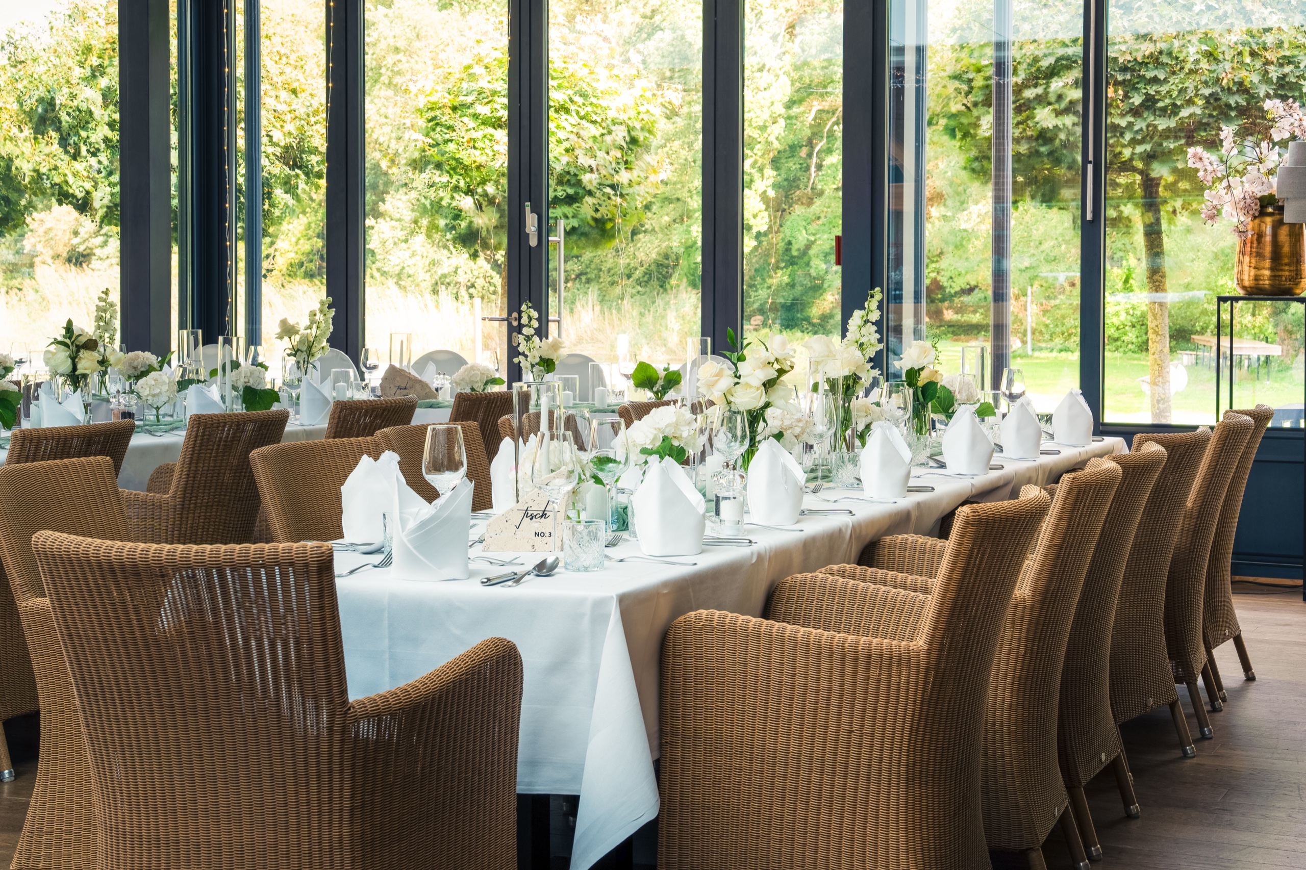 Gedeckte Tafel mit weißen Blumen im Wintergarten auf Gut Altona, dahinter der Garten