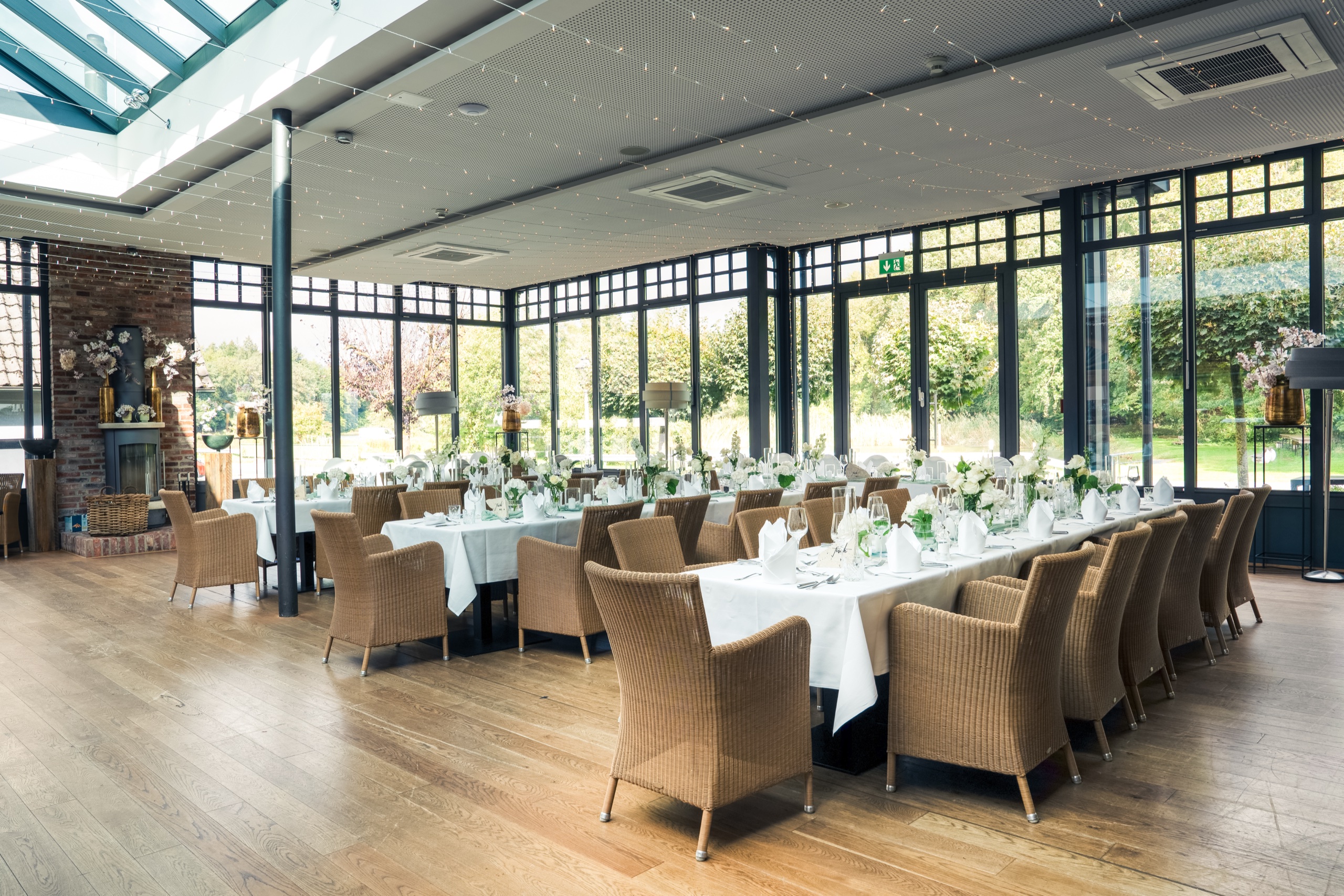 Wintergarten auf Gut Altona mit langen Tafeln, Korbstühlen und Glasdach